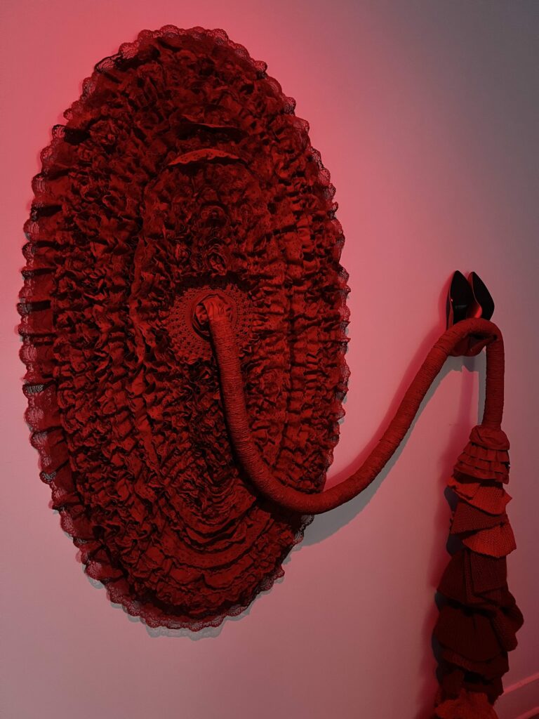 An art sculpture with high heels, beading, knitted fibers and a variety of objects. 