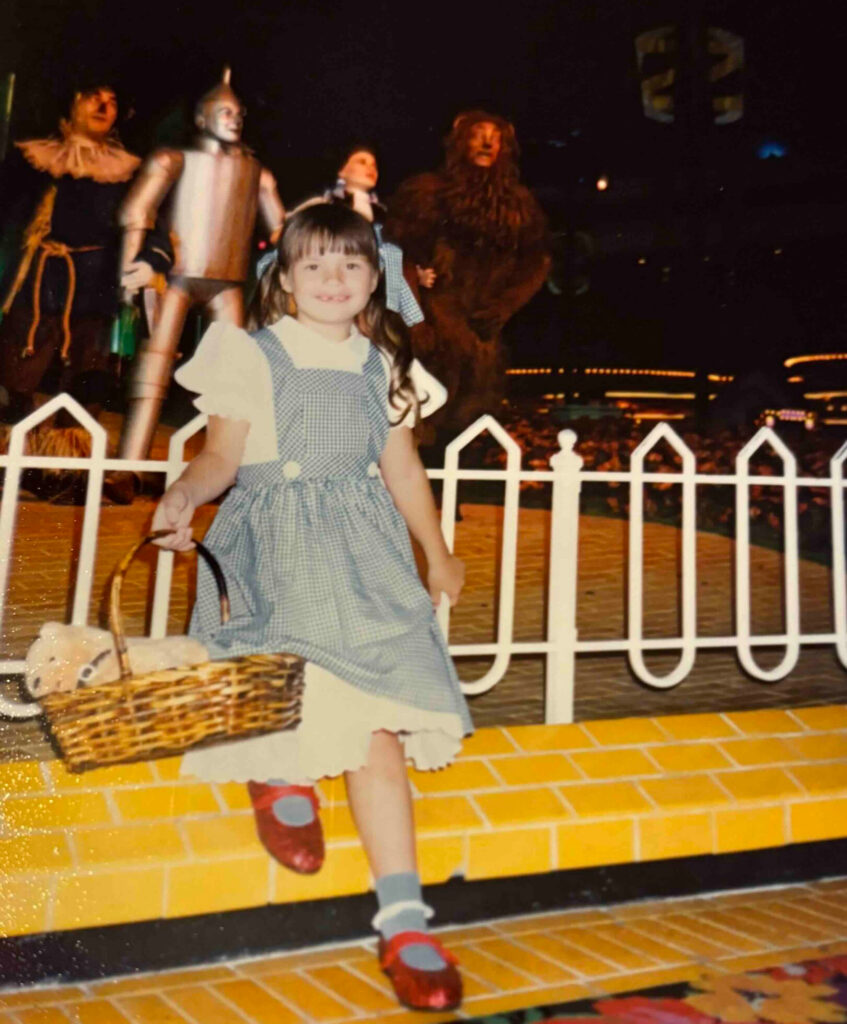 A little girl dressed as Dorothy from The Wizard of Oz smiling at the camera.