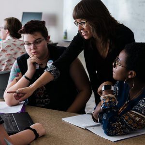 Professor points at laptop with three students