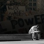 Photo of man reading alone on a bench with protest image overlaid on background