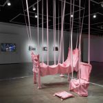 pink sculpture in the middle of the gallery with a tv and framed photos behind on a wall