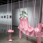 pink sculpture in the middle of the gallery with a green sculpture and framed photos behind on a wall