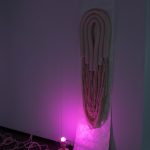 sculpture hanging on wall and draped onto floor with pink light