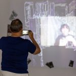 person holding a cell phone taking video of an art installation