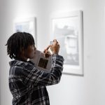 person holding a cell phone taking a picture of a framed photograph on a gallery wall