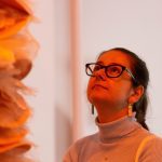 person looking up at a sculpture with orange light