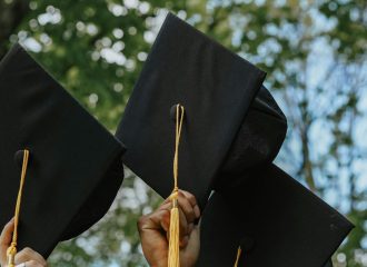 Three hands displayed holding graduation caps.