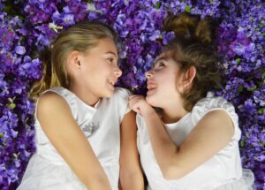 Hailey and her sister Livy are pictured as children, laughing together in a bed of purple flowers. They are wearing matching white outfits.