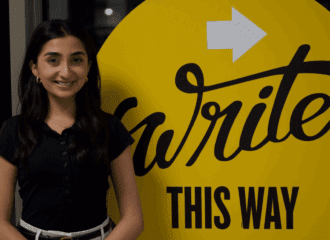 A professional photo of Shivani Vakharia in front of a UWC sign reading "Write This Way"