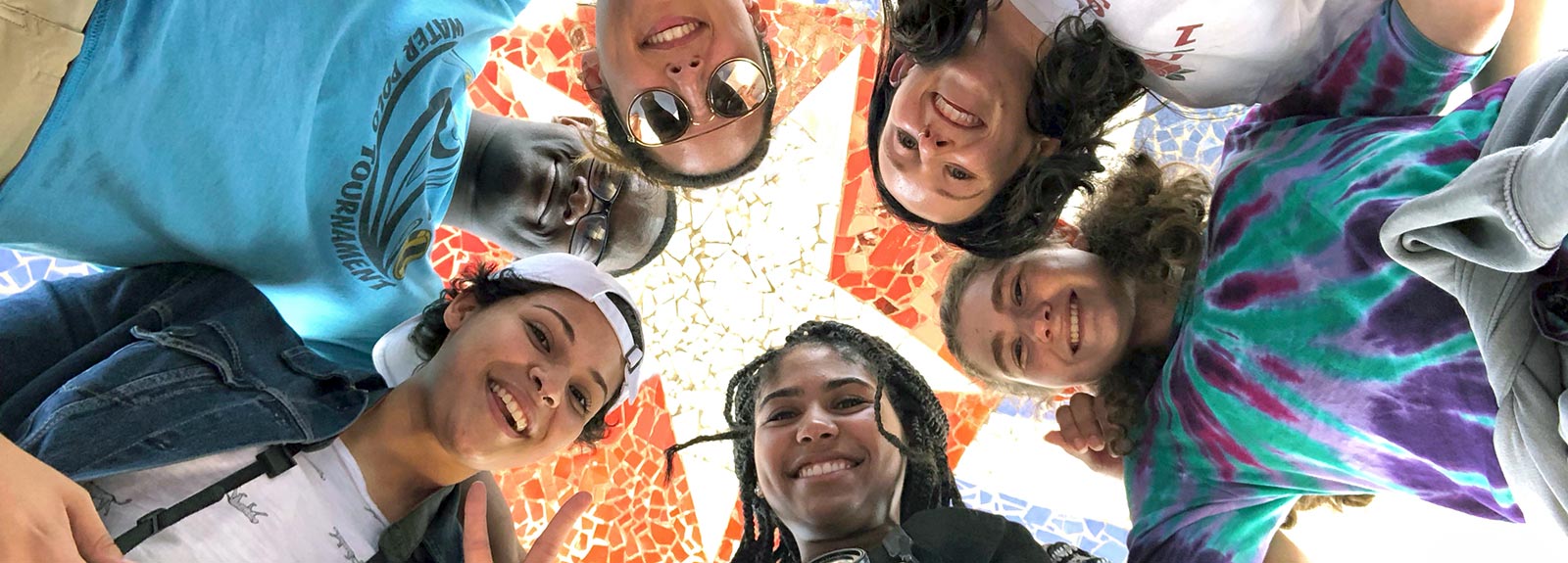 A group of smiling students pose in front of a mosaic featuring the Cuban flag