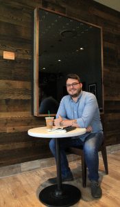 Photo of UCF alumnus Forrest Lawson '18 in front of his art at the Starbucks on Memory Mall
