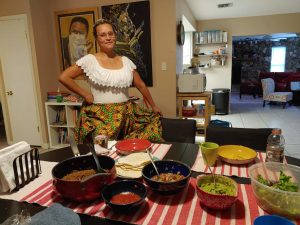 Contributing artist Wanda Raimundi-Ortiz poses in traditional clothing with the Puerto Rican food she made for her family