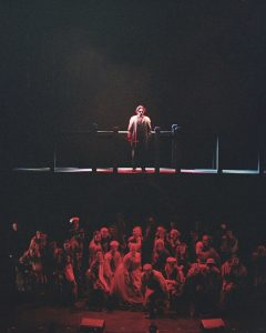 Image of Sweeney Todd standing above the ensemble, immersed in red, ominous lighting.
