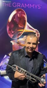 Carl Fischer holding a trumpet in front of a backdrop that says "CBS presents The Grammys"