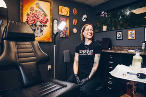 Stacie Becker sitting in her tattoo studio, Empower Tattoo, smiling at the camera.