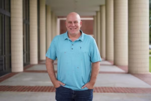 Jason Durrell wearing a blue collared shirt, with his hands in his pockets smiling at the camera.