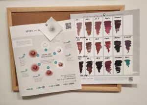 Printed medical tattoo reference materials pinned to a corkboard, showing areola tattooing steps and ink color swatches.