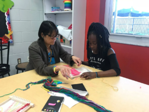 Dr. Stella Aunt helps a third grader during UCF CREATE's weaving and dyeing summer camp.