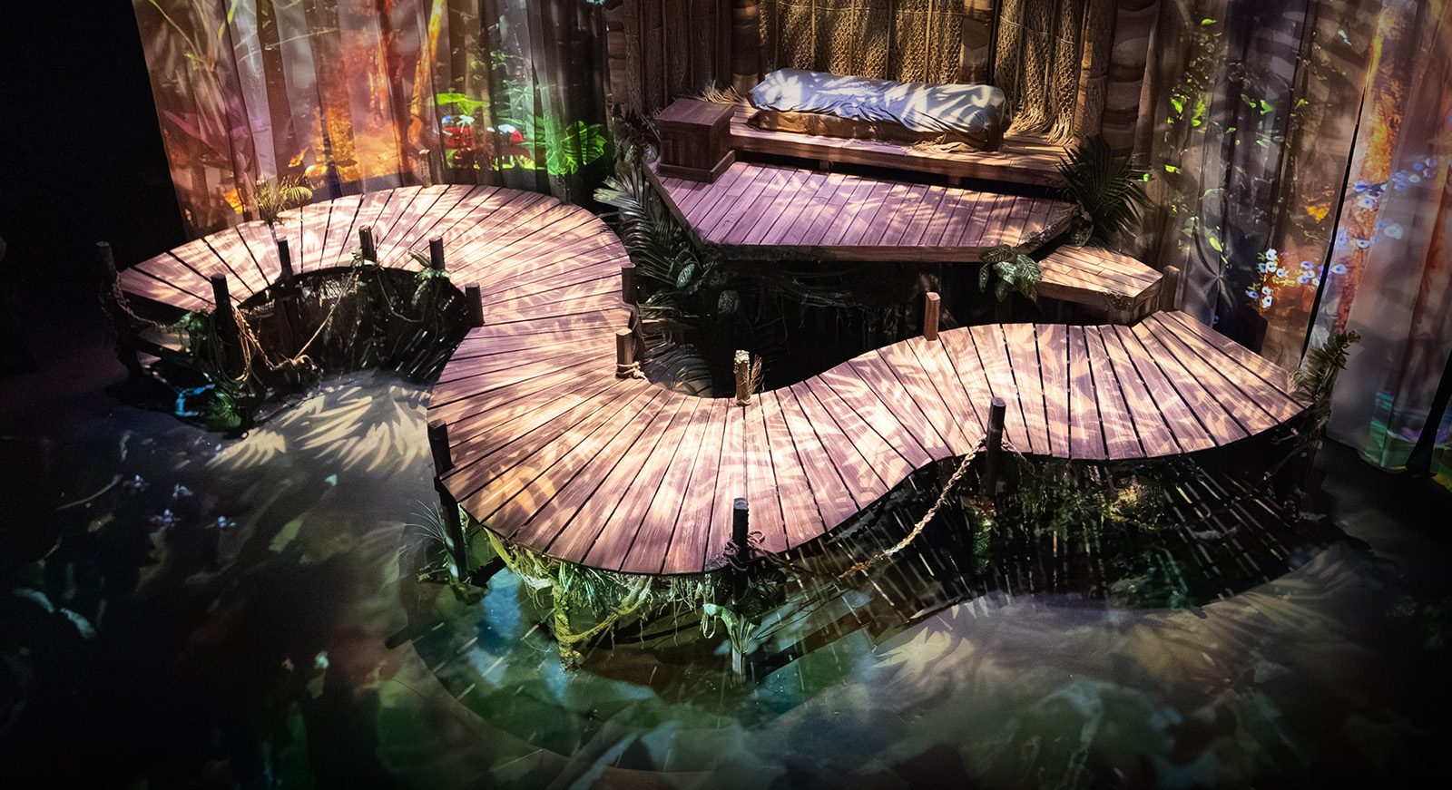 Theatrical set featuring a dock in the jungle with complex projection overlays.