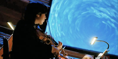 Student violinist performs in front of video screen