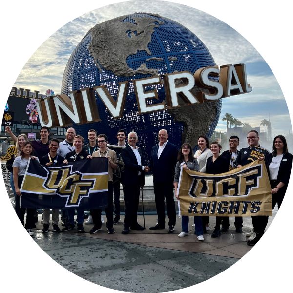 Outside the Universal Studios entrance, UCF’s Themed Experience Program Director Peter Weishar shakes hands with Universal Creative President Mike Hightower while surrounded by a group of UCF students interning with the company.