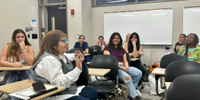 Photo of female students sitting in a classroom engaging in conversation with each other