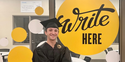 Student standing in front of sign that says Write Here