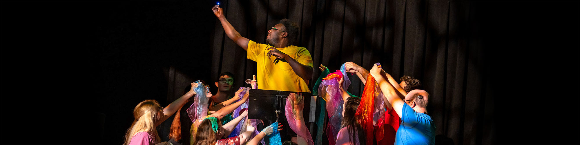 Group of actors in colorful shirts reach upward