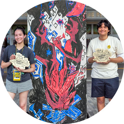 Students stand next to their artwork holding trophies