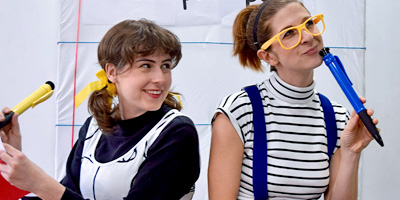 Two student performers pose iwth oversized pens