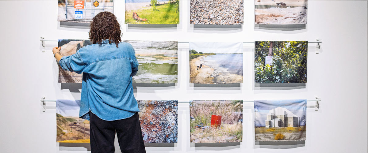 Artist hangs a collection of works on a white wall.