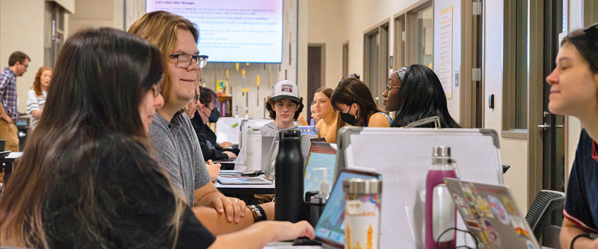 Many students work and converse at tables in the writing center