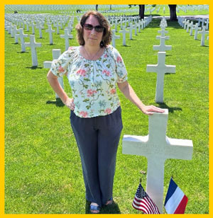 Associate Professor of History Amelia Lyons poses next to a cross-shaped headstone in a cemetery.