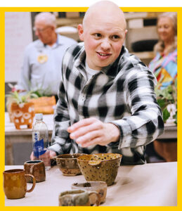 Student leans over a table with handmade ceramic wares