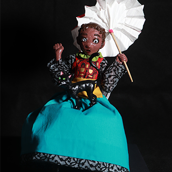 A doll or sculpture stands gracefully holding a white parasol, dressed in a flowing turquoise dress and patterned shirt, created by Savannah Ryan.