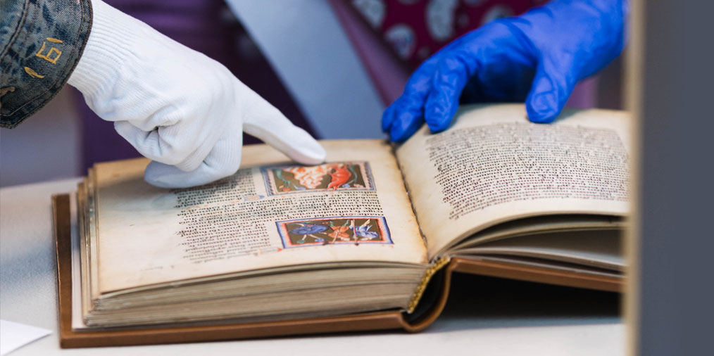 Gloved hands examining illuminated manuscript