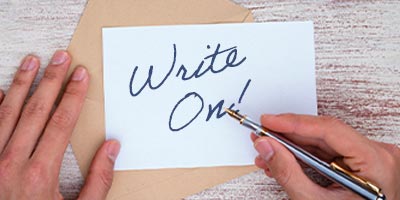 Hands writing 'Write On!' on a notecard